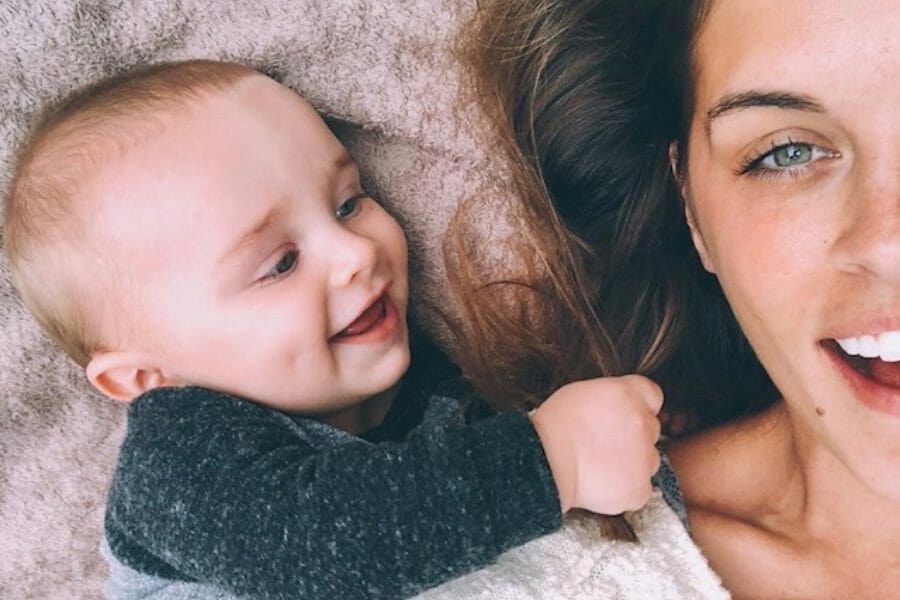 mom lying on floor smiling with baby tugging her hair and smiling at her