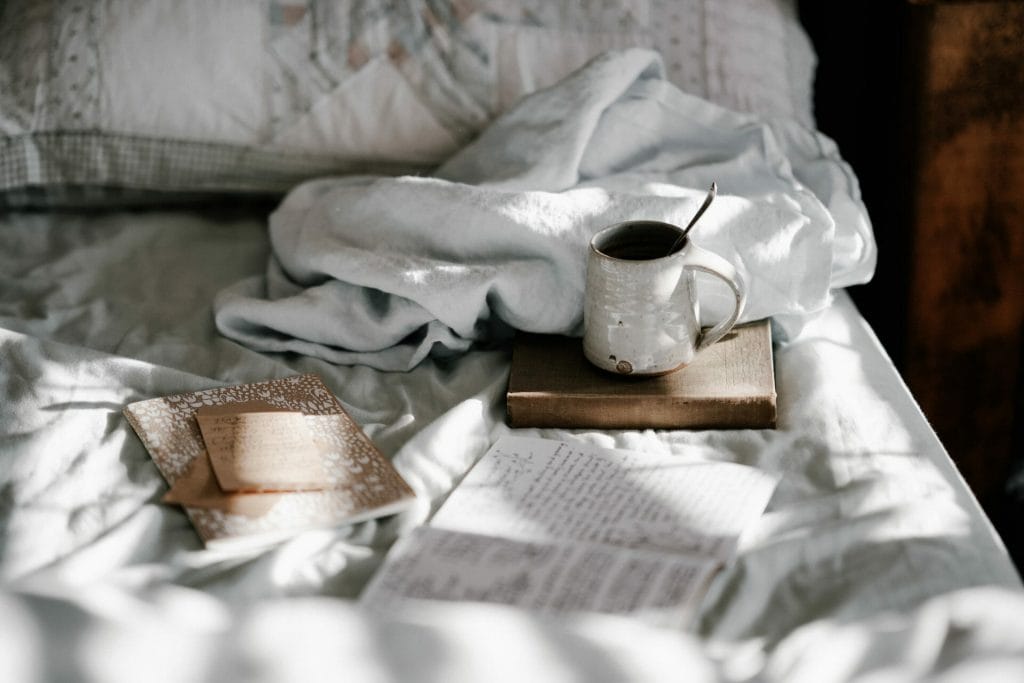 cozy bed with white linens, a journal, and a mug