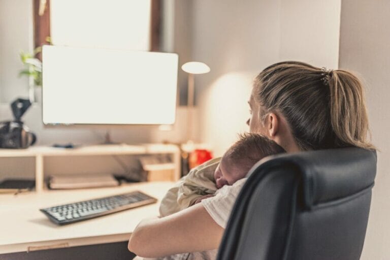 mom sitting at computer desk working with infant on her shoulder