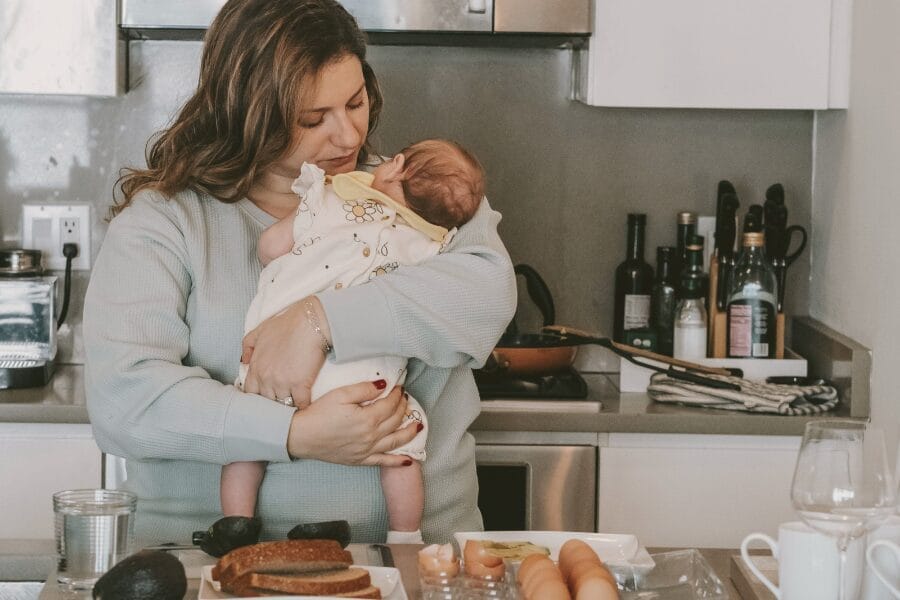 mom holding newborn making breakfast