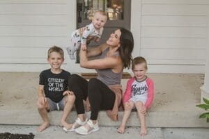 mom with three kids on porch holding up baby mom goals